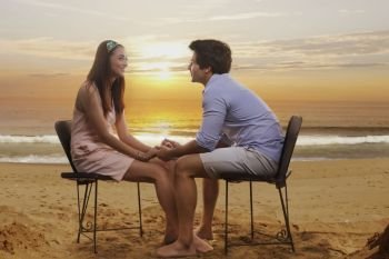 Couple sitting in chairs holding hands on beach at sunset