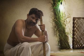 Portrait of male farmer sitting indoors holding stick