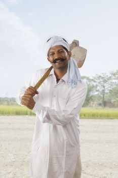 Farmer carrying hoe on his shoulder standing in field