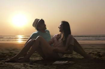 Smiling young couple sitting together on beach at sunset