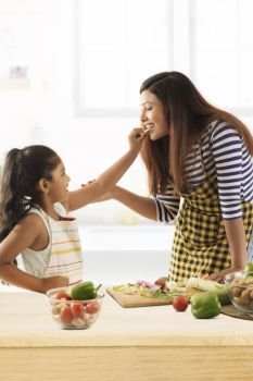 Daughter feeding cucumber to her mother in kitchen
