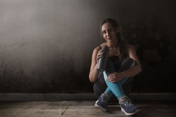 Female runner sitting legs crossed on floor holding water bottle