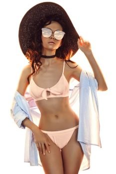 Sunny fashion photo of beautiful slender woman in pink bikini and black hat. Beach summer vibes