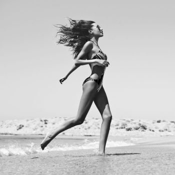 Black and white outdoor fashion photo of beautiful happy slender woman running on sea. Beach travel. Summer vibes
