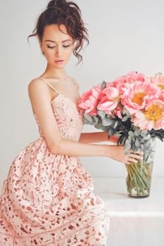 Home stylish fashion photo of beautiful young woman in lace dress with big bouquet of peony. Holidays and Events. Valentine’s Day. Spring blossom. Summer season.