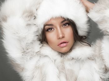 Fashion studio portrait of beautiful lady in white fur coat and fur hat. Winter beauty in luxury. Fashion fur. Beautiful woman in luxury fur coat. Fashion model posing in eco-fur coat and eco-fur hat