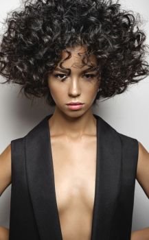 Fashion studio portrait of beautiful woman in black vest with afro curls hairstyle. Fashion and beauty