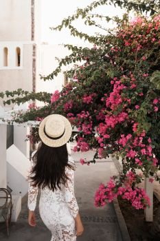 Happy woman in white dress and straw hat enjoying her holidays on Santorini island. View on Aegean sea from Oia. Europe summer travel destination. Greek Islands