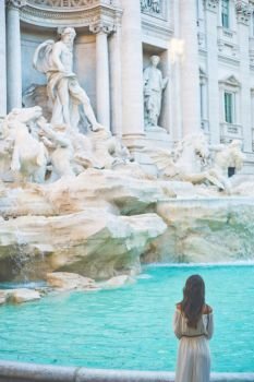 Beautiful woman in white dress sitting in front of Trevi Fountain, Rome, Italy. Happy woman enjoy italian vacation. Holiday in Europe.. Woman in white dress  in front of Trevi Fountain in Rome
