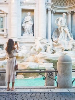 Beautiful woman in white dress take a photo of Trevi Fountain, Rome, Italy. Happy woman enjoy italian vacation. Holiday in Europe.. Woman in white dress  in front of Trevi Fountain in Rome