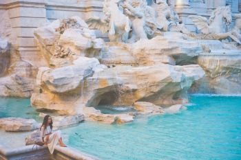 Beautiful woman in white dress sitting in front of Trevi Fountain, Rome, Italy. Happy woman enjoy italian vacation. Holiday in Europe.. Woman in white dress  in front of Trevi Fountain in Rome