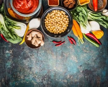 Vegetarian cooking ingredients with chick peas dish, spicy indian curry paste , greens, ginger and vegetables on rustic background, top view, border.  Healthy food and eating or Indian cuisine concept
