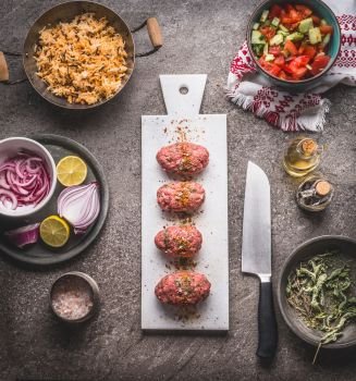 Raw Meat balls on white cutting board on kitchen table background with knife , rice pot and salad dish , cooking preparation , top view. Healthy and clean food and eating  concept.