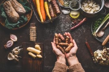 Female woman hands holding jerusalem artichokes or earth pear vegetables on rustic kitchen table with vegetarian cooking ingredients and tools. Healthy and clean food  cooking and eating  concept.