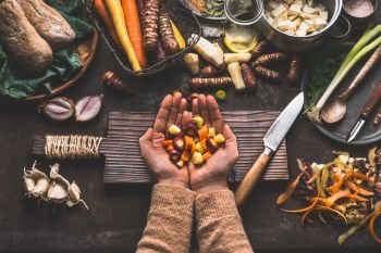 Female woman hands holding diced colorful vegetables on rustic kitchen table with vegetarian cooking ingredients and tools. Healthy and clean food  cooking and eating  concept.