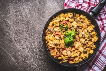 Tasty vegetarian tortellini pasta pot with vegetables sauce on rustic background , top view. Italian cuisine food concept