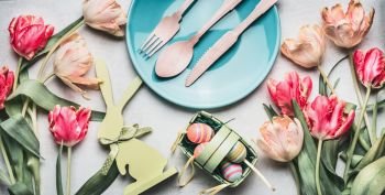 Easter composing with spring tulips , bunny decor, eggs and festive table setting with plate and cutlery, top view, banner