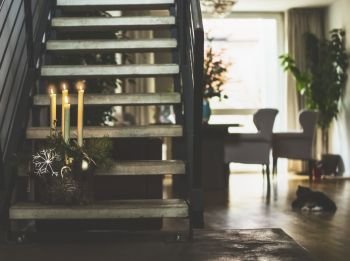 Cozy living room with stairs to second floor , winter decoration with burning candles on steps, window and cat. Winter holiday atmosphere at home. Fourth Advent wreath .