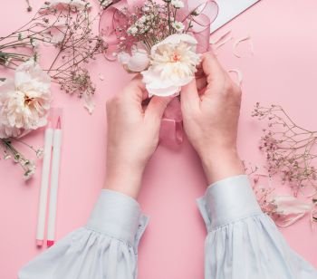 Female hands making floral arrangements with white flowers  at pastel pink background, top view