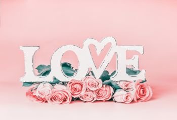 Word LOVE on pastel pink background with roses bunch, front view. Creative female holidays layout with copy space for greeting