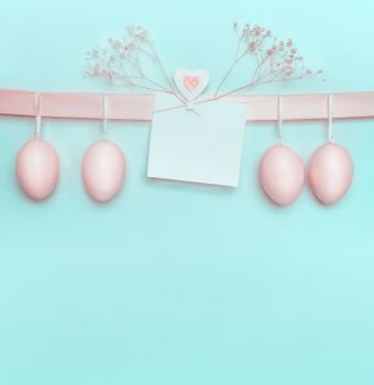 Easter greeting card with pastel pink eggs hanging on ribbon on light  blue turquoise background. Creative greeting concept. Layout with copy space for your text