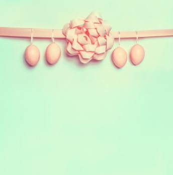 Pastel pink Easter eggs hanging on ribbon with beautiful bow on light green background. Creative greeting layout with copy space for your text