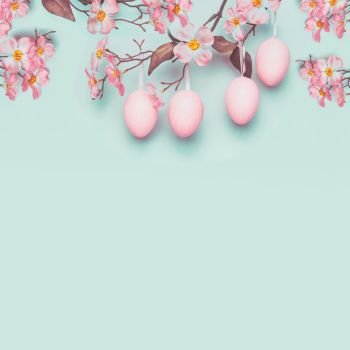 Easter layout with hanging pastel pink eggs and spring blossom at light at blue turquoise background. Copy space for greeting or invitation