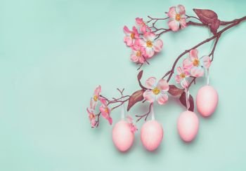Pastel pink Easter eggs hanging on spring blossom branch at blue turquoise background, copy space for greeting or invitation