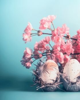 Easter eggs in crate box with decorative spring blossom at blue background, front view