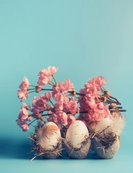 Easter eggs in crate box with decorative spring blossom at blue background, front view, pastel styled