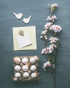 Easter greeting layout composing with eggs, blossom and blank card mock up on gray background, top view, flat lay