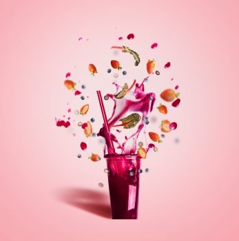 Glass with drinking  straw and purple splash summer beverage: smoothie or juice with flying berries ingredients on pink background, front view