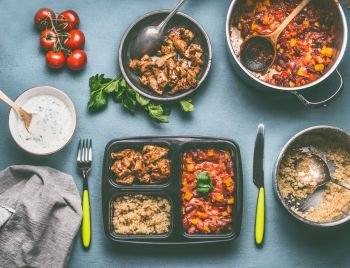 Healthy balanced lunch box preparation with quinoa, tomatoes beans sauce and chicken meat on kitchen table background with food pots and bowls, top view