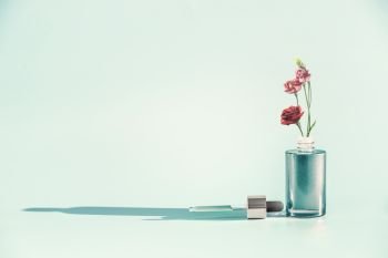 Herbal skin care cosmetics and beauty concept. Facial Serum or Oil bottle with dropper or pipette and flowers stand at  blue background, front view. Modern minimal creative layout