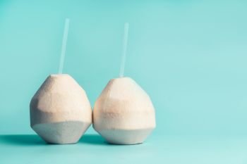Fresh coconut cocktails  with pink drink straw at blue turquoise background, front view. Healthy coconut water