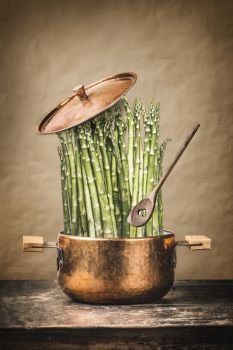 Asparagus in cooking pot with wooden spoon on rustic table , front view.   Healthy vegetarian food and eating concept