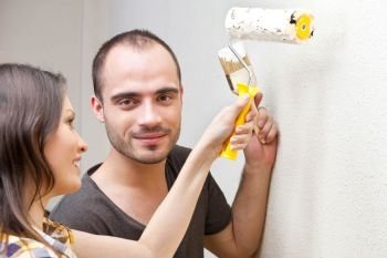 Young couple painting a wall with roller and doing repair at home together