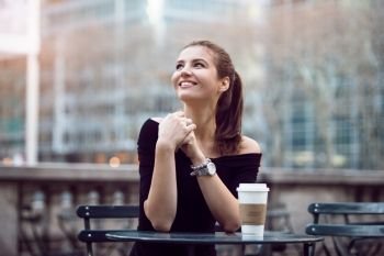 Beautiful happy businesswoman sitting in city park during lunch time or coffee break with paper coffee cup. Woman with coffee smiling outdoors.