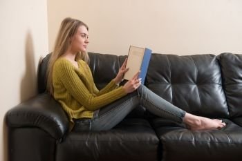 Woman reading a book and sitting on sofa at home