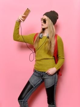 Hipster girl taking selfie on mobile phone and listen music wearing street style casual outfit with jeans an sunglasses. 