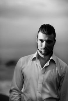 guy with a beard against the sea in the evening in a white shirt, portrait