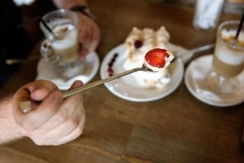 the groom holds the spoon meringue with strawberries on the background of the table with coffee