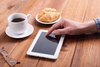 Man with digital tablet croissants and coffee on a wooden table.