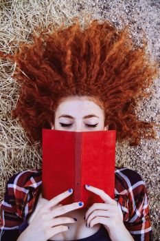 Young redhead woman covering by a book 