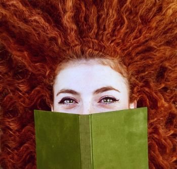 Young redhead woman covering by a book 
