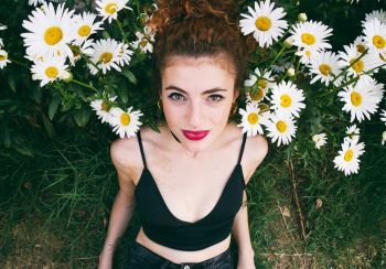 Young redhead woman surrounded by daisies 