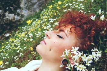 Close up of a young and redhead woman sleeping in a field of flowers 