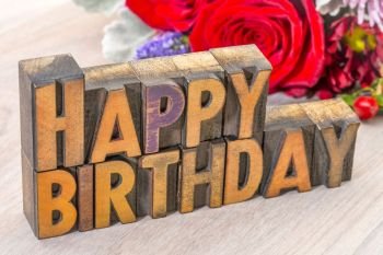 Happy Birthday greeting card in vintage letterpress wood type against grained wood with flowers