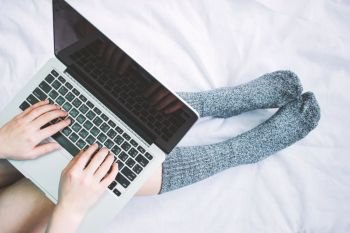 Top view of woman legs in socks and using laptop on cozy bed, lifestyle concept