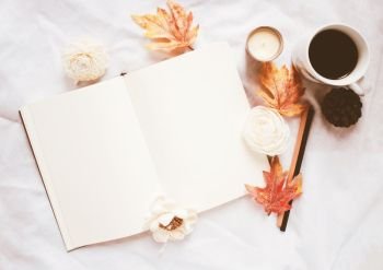 Autumn lifestyle concept, blank notebook and coffee with autumn leaves ornaments on white bed sheet background